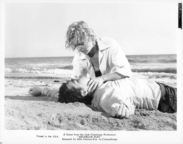 Tuesday Weld helping an unknown actor that is laying in the sand i- Old Photo